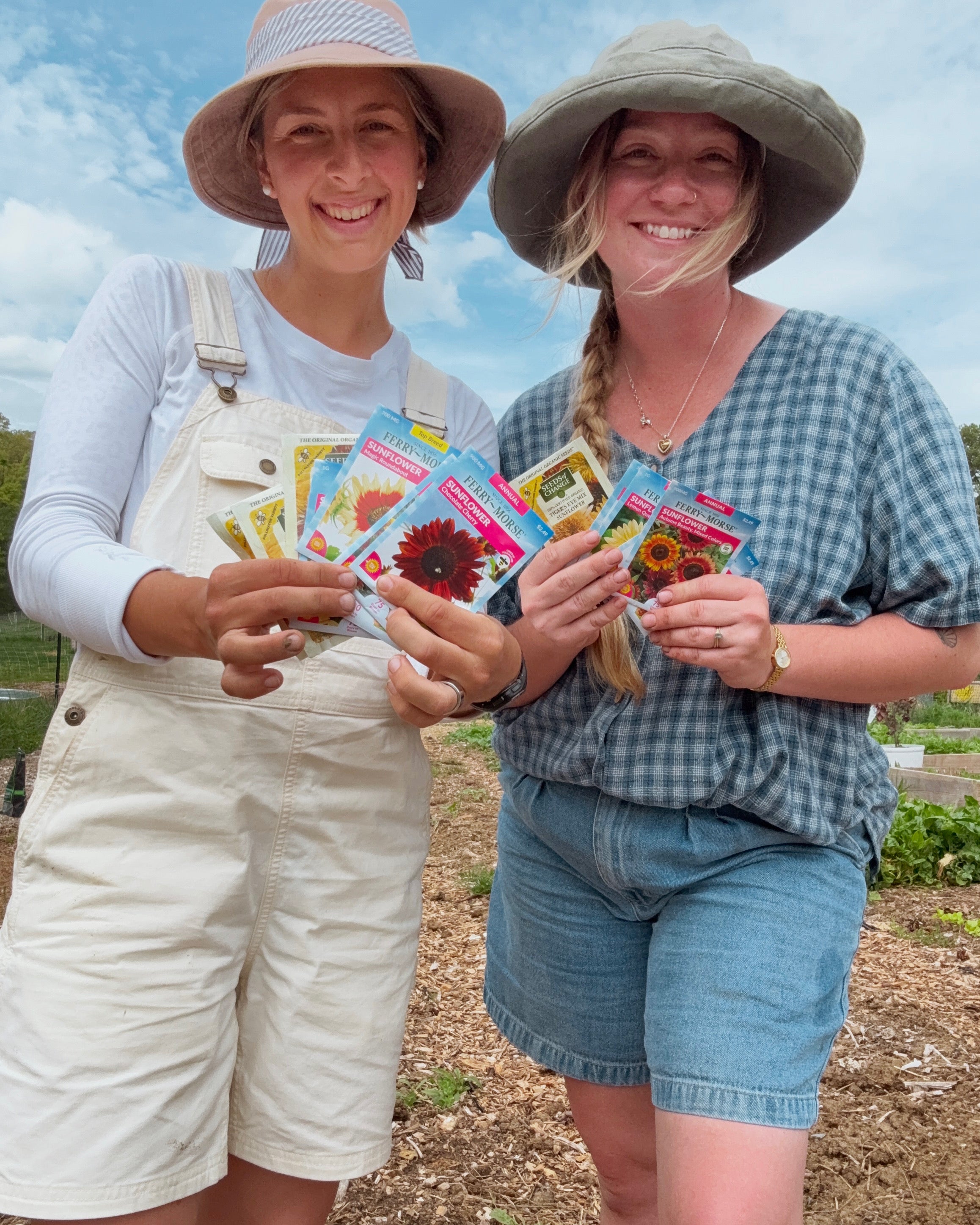 Two women holding seed packets in a garden setting