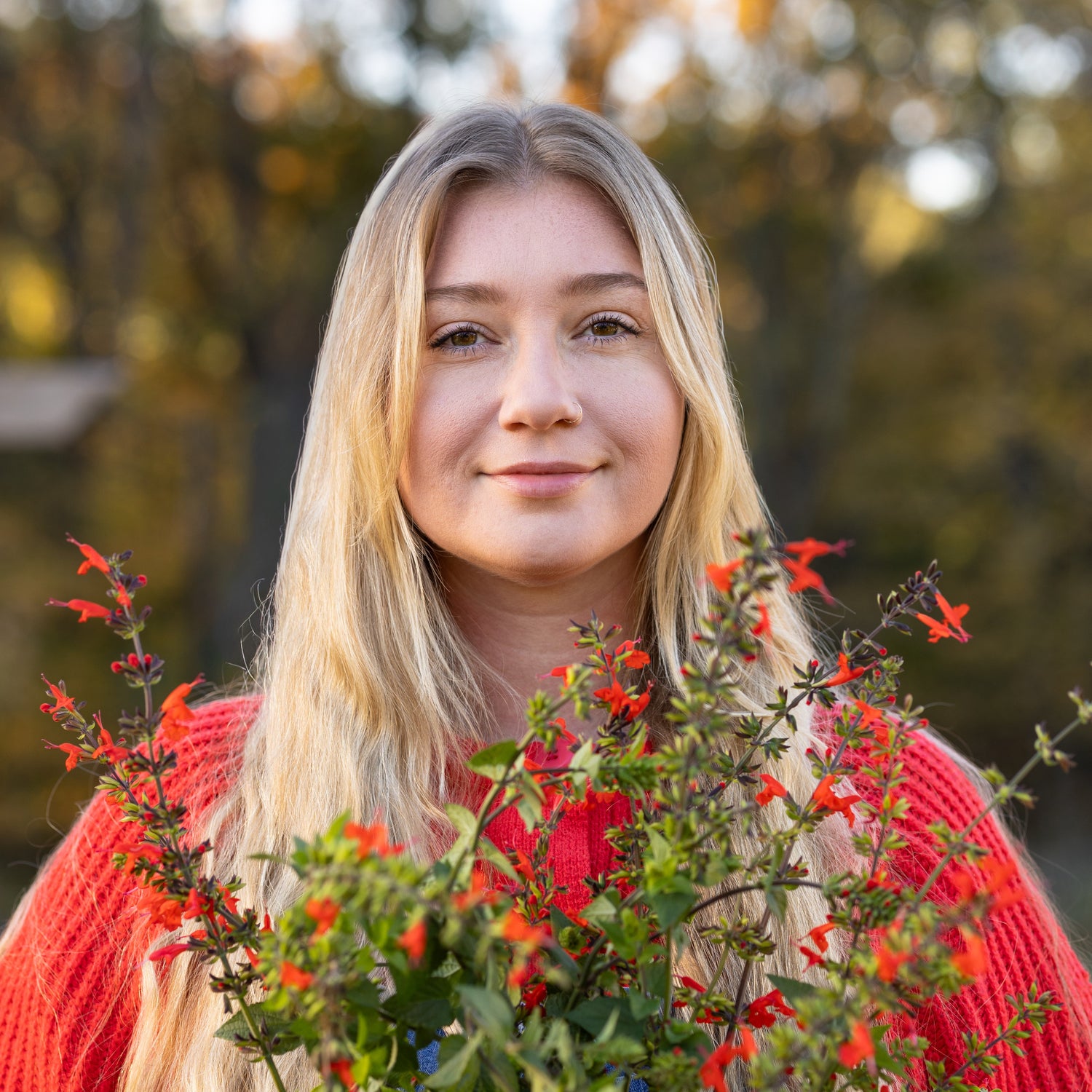 Blonde Woman holding a bouquet of red flowers outdoors with blurred trees in the background